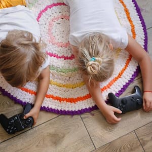 Two siblings laying on a rug on a laminate floor playing videogames