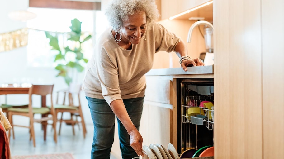 A smiling woman keeping plates in dishwasher