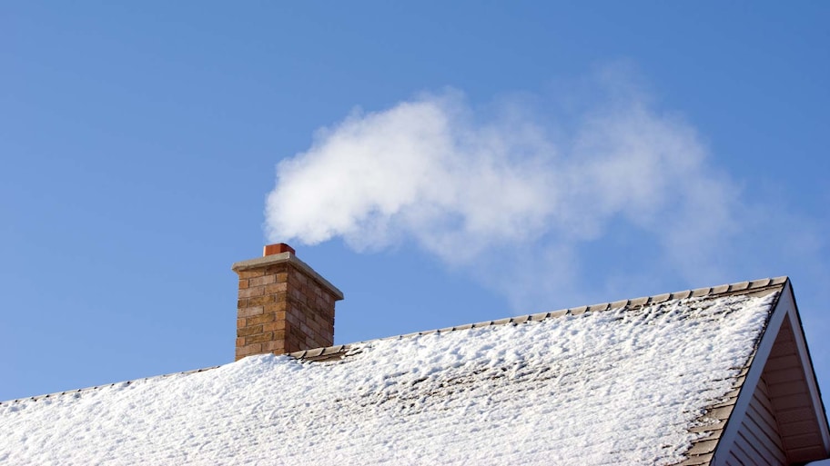 A snow covered roof with smoke coming out of the chimney