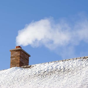 A snow covered roof with smoke coming out of the chimney