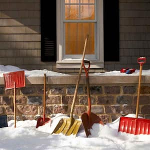 Snow shovels lined up against the side of a house