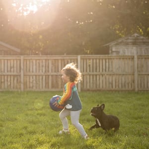 A toddler holding a football running along her father and her dog in the garden