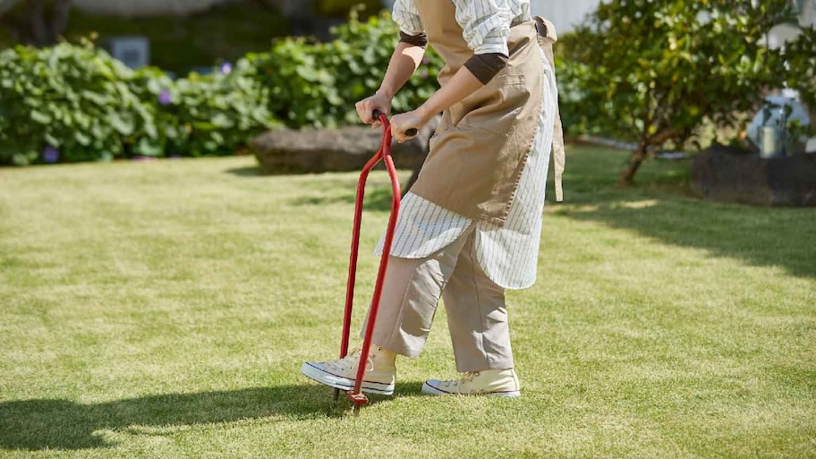 A woman doing manual core aeration on lawn