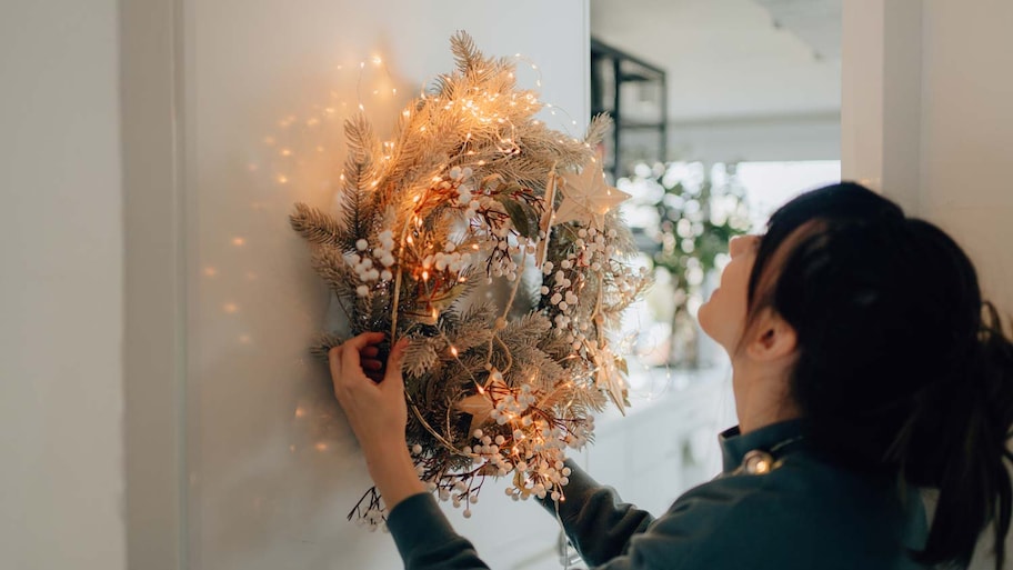 A woman hanging a wreath with lights