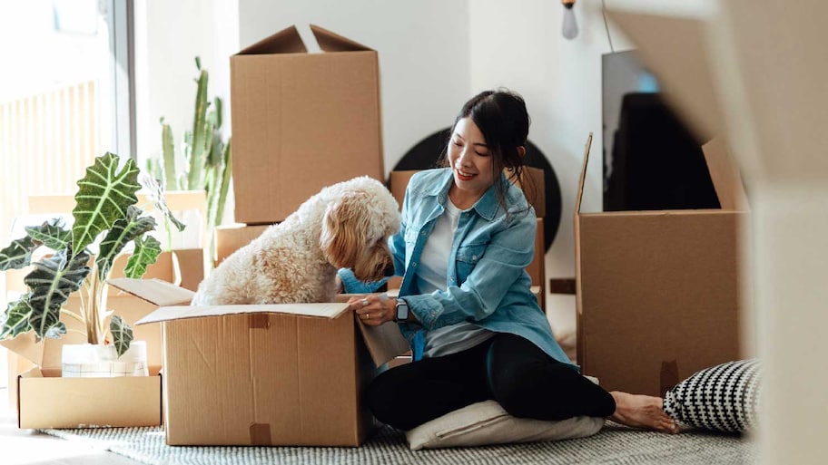 A woman having fun with her dog while packing moving boxes 