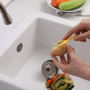 A woman peeling vegetables over a garbage disposal