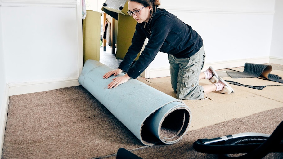 Woman rolling up old carpet in preparation to renew flooring