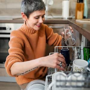 Mature woman with tattoos putting dishes in dishwashe