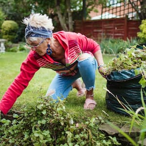 Senior woman gathering weeds and garden waste in her compost bag