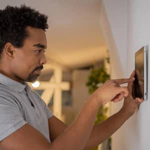 A young man adjusting the thermostat in his house