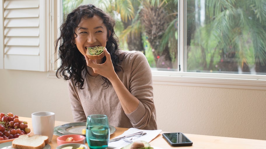 A young woman eating avodaco toast in her kitchen