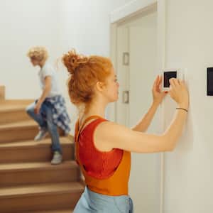 A young woman turning on a thermostat