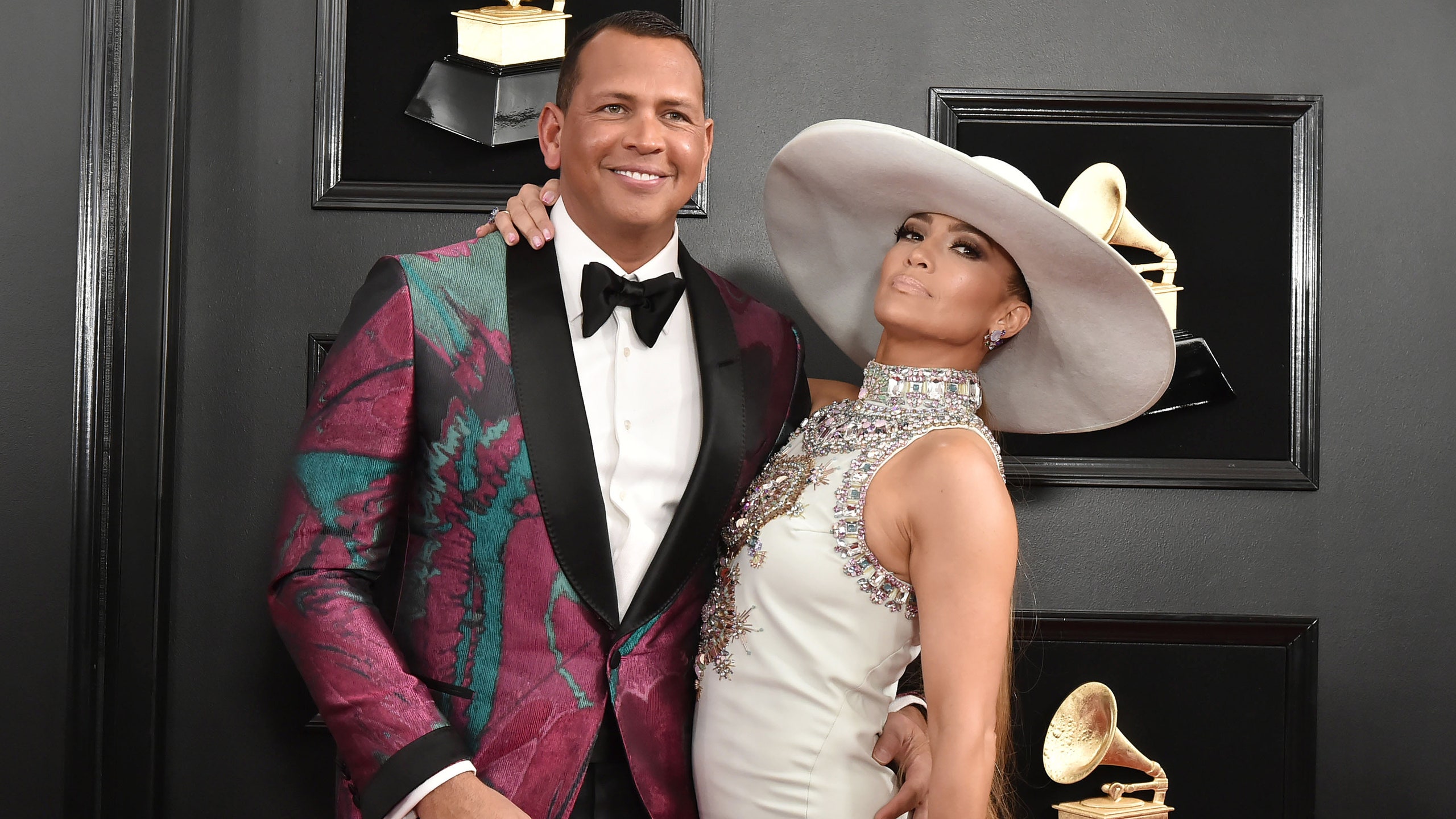 woman in white dress and hate with arm around man in multicolored tuxedo