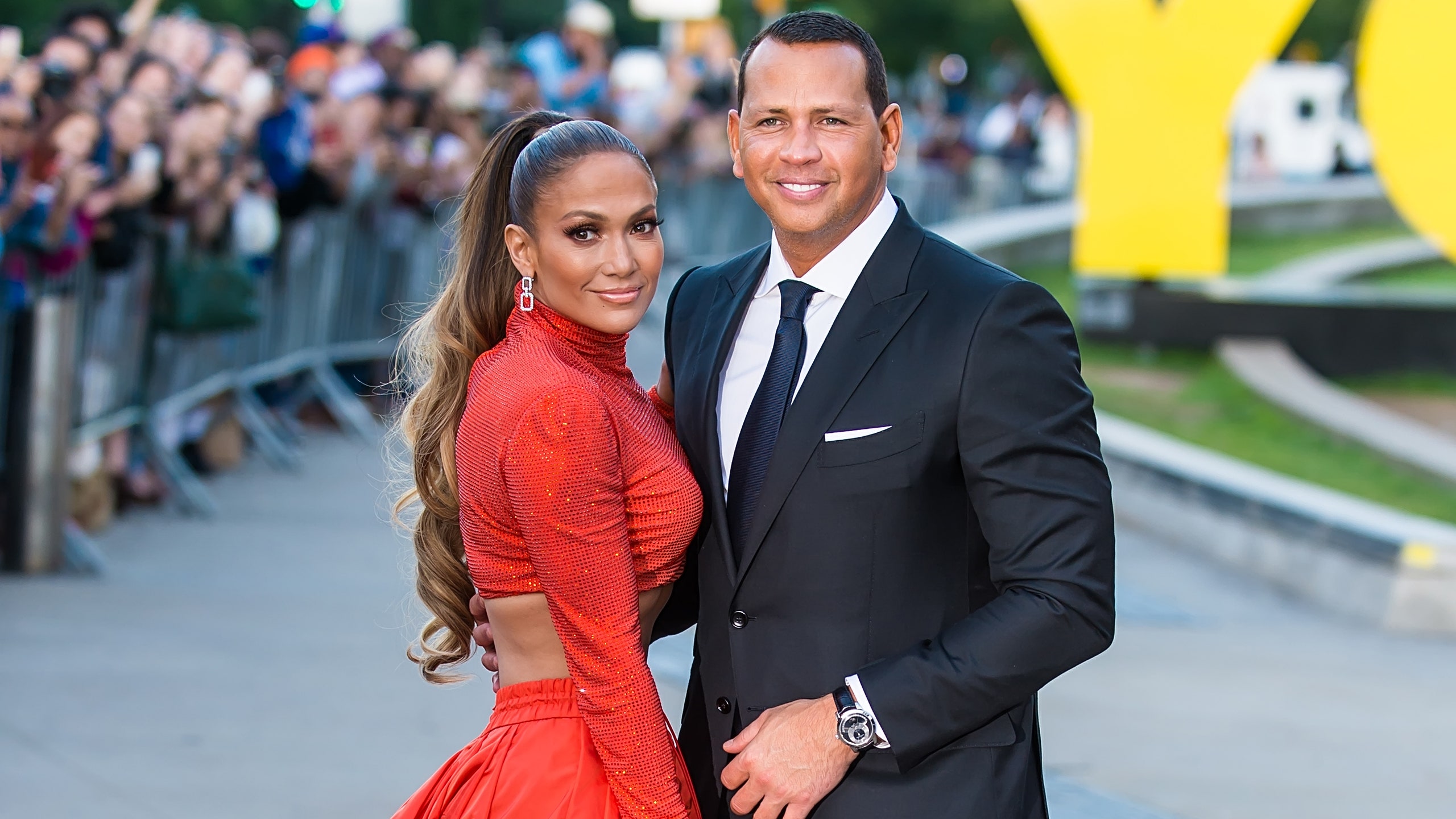 a woman in a red skirt and red long sleeve top with a long brown ponytail standing with a man in a suit