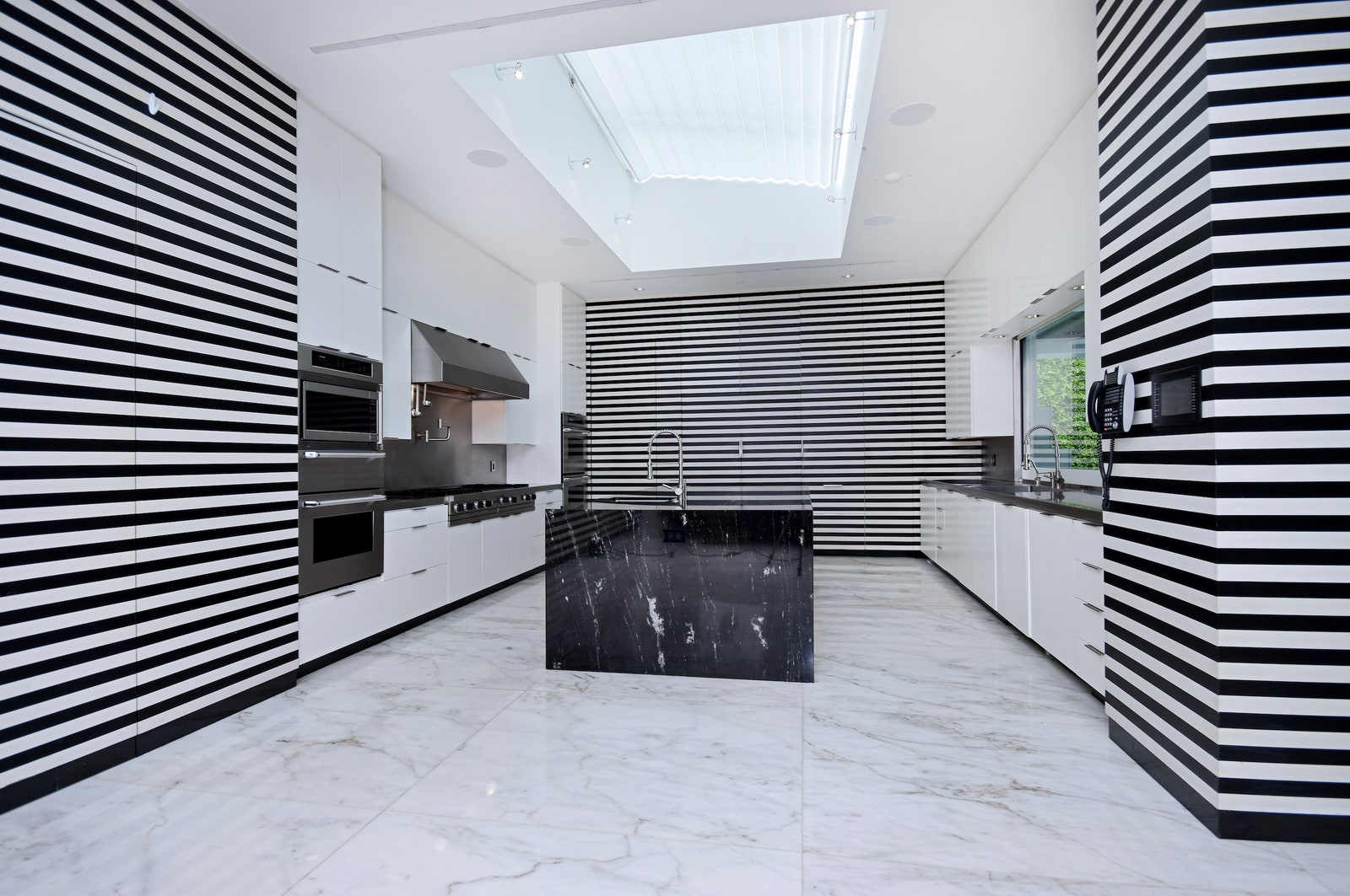 a kitchen with white cabinets a white marble floor a black marble island and black and white striped walls