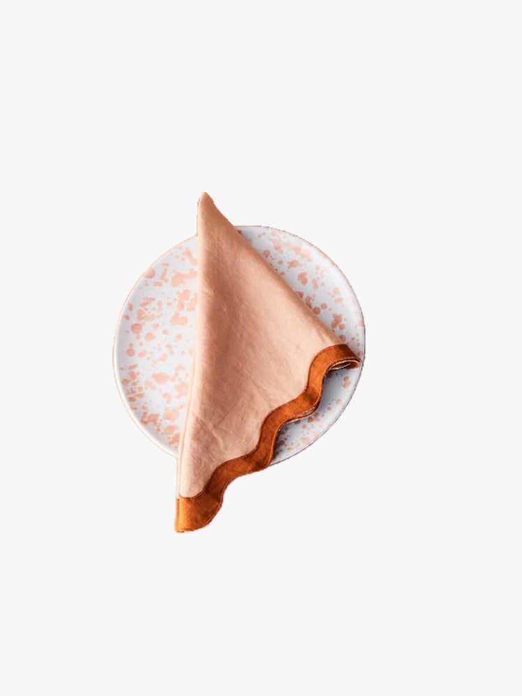 Pink and orange napkin with a scalloped edge on top of a splatter painted plate.