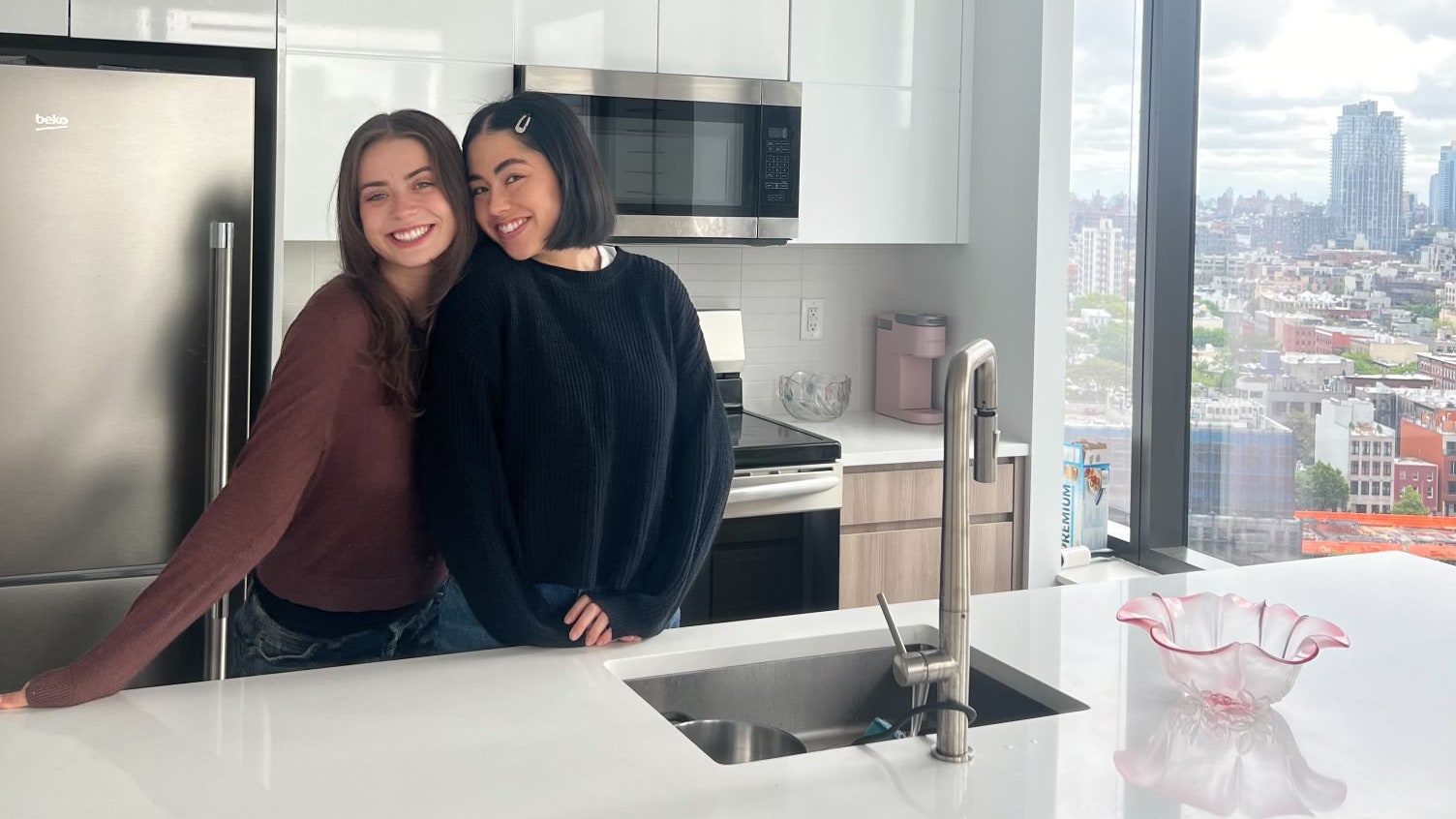 two women standing at white kitchen island secured through the NYC housing lottery white cabinetry steel refrigerator...