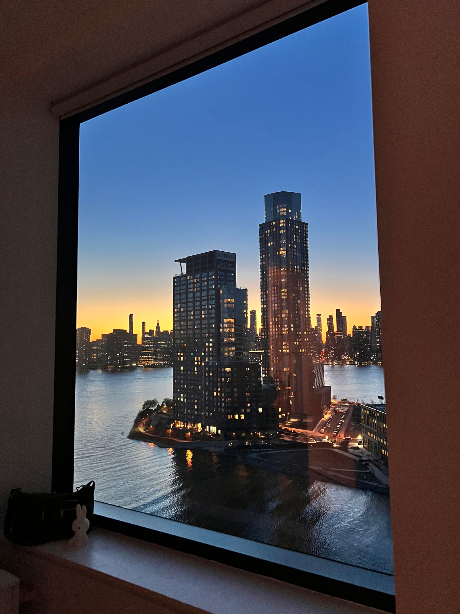 window through which building lit up in foreground NYC skyline in background is visible at twilight