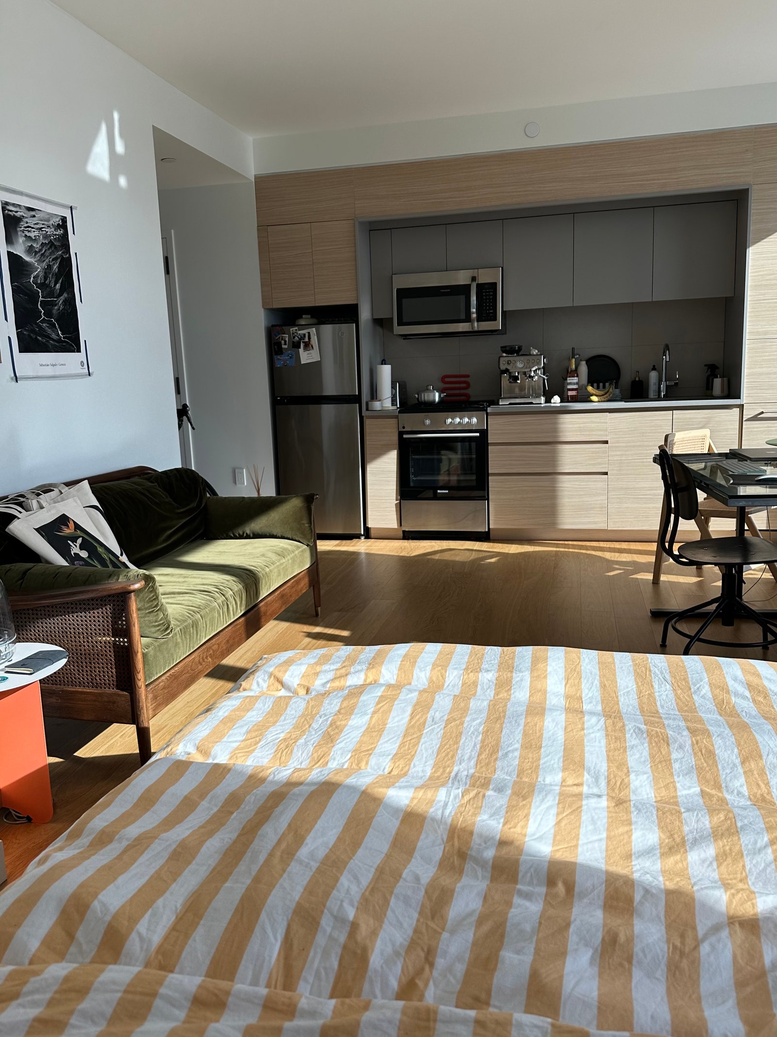 striped yellowandwhite duvet in foreground green sofa in wood frame to left kitchen space in far background desk to right