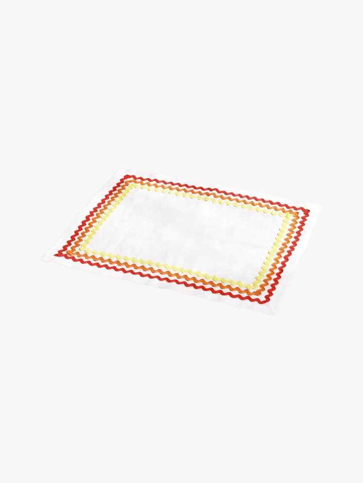 White linen placemat with border of red orange and yellow zigzag stitching.