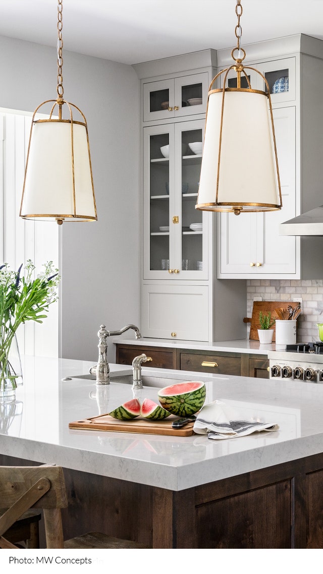 Kitchen island with white countertop and two cylindrical pendant lights hanging above it.