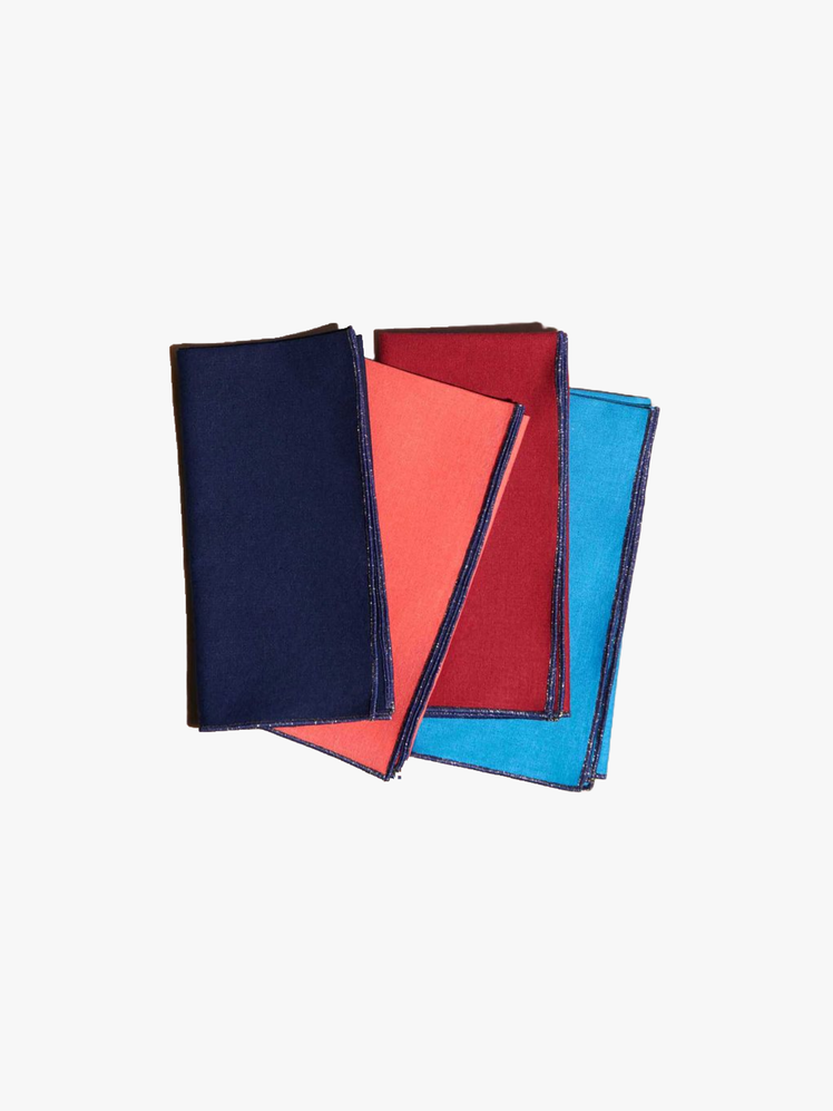 Four jeweltoned linen napkins with navy stitching on the edges folded in a pile.