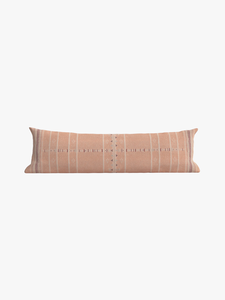 A lumbar pillow in a blush hue with ornate cream and redcolored detailing.