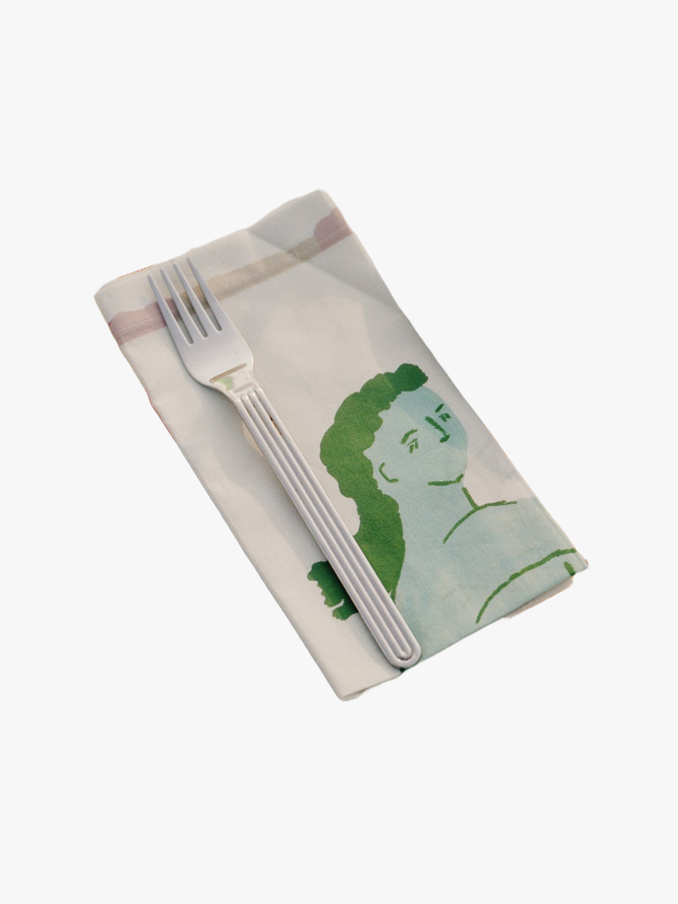 Folded cloth napkin featuring an illustration of a mythical Siren in green with a fork laid on top.