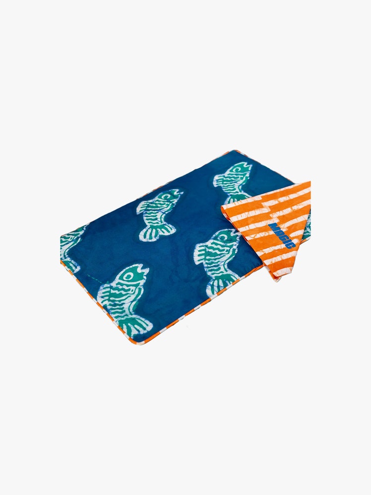 Doublesided batik printed placemat. One side features a blue fish pattern and the other an orange and white stripe.