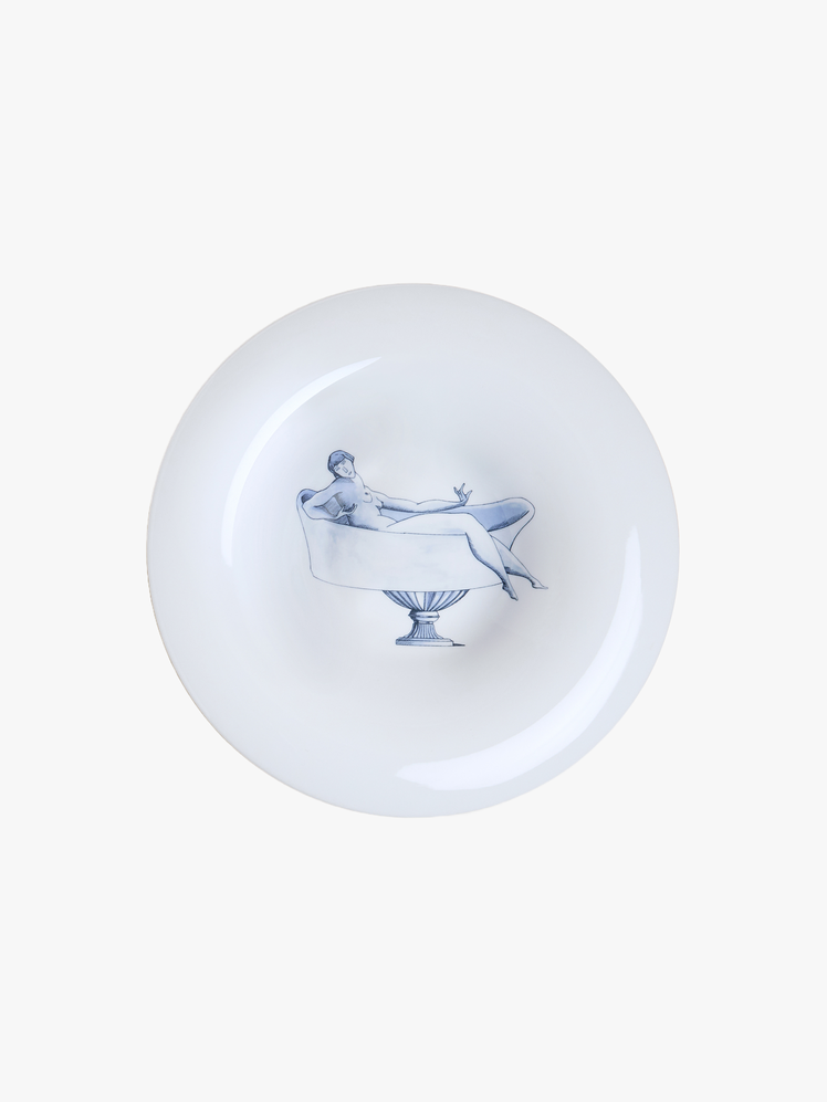 White porcelain plate featuring a painting of a woman reclining in a bathtub in blue glaze.