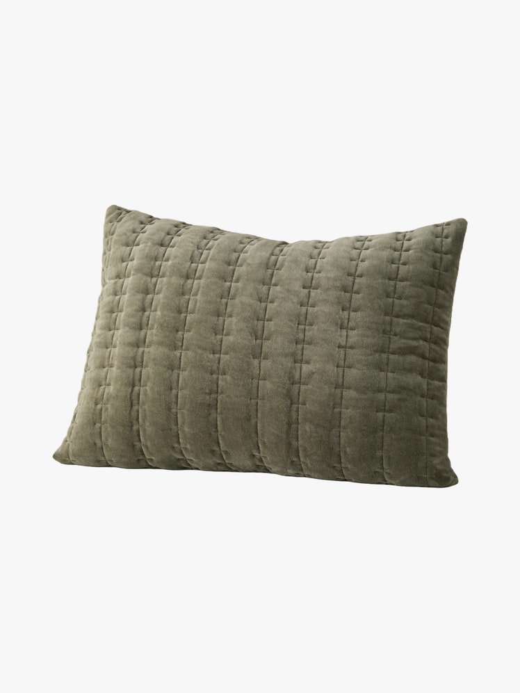 Rectangular pillow with a green velvet cover with vertical lines of quilted stitching details along it.