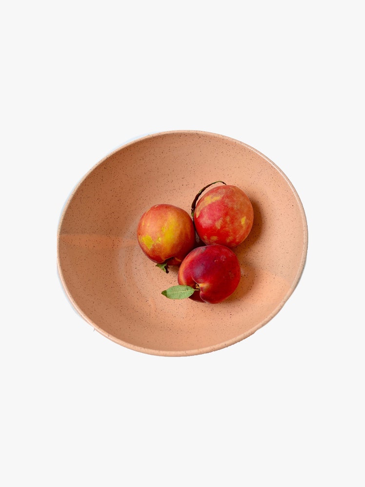 Light orange speckled ceramic bowl with three peaches inside.