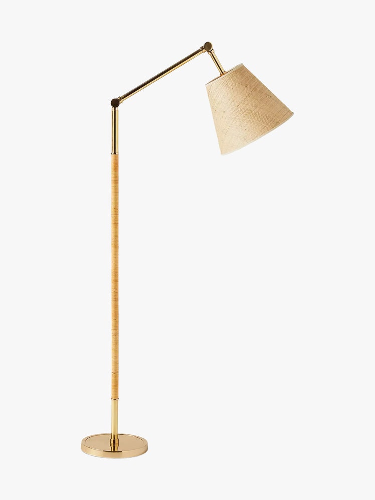 Floor lamp with a brass base rattan wrapped pole and an adjustable arm finished by a raffia taper shade.