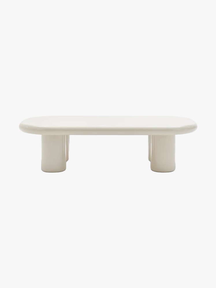 White coffee table with an oval shaped tabletop cylindrical legs anda  highgloss finish.