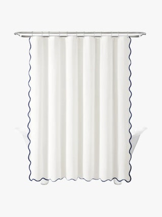 White shower curtain with a navy scalloped edge hanging above a bathtub.