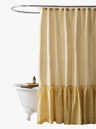 Yellow shower curtain with a striped pattern and a thistle print on a ruffled bottom edge hanging over a bathtub.