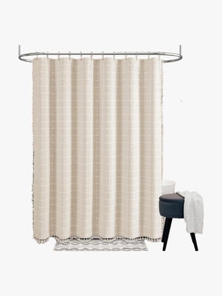 Beige embroidered plaid shower curtain with tassels on three edges hanging above a bathtub.