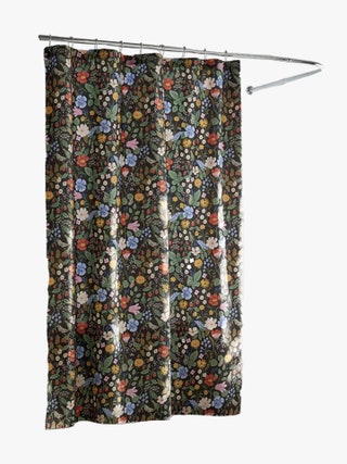 Black shower curtain with a multicolored floral print hanging rom a curved silver shower rod.