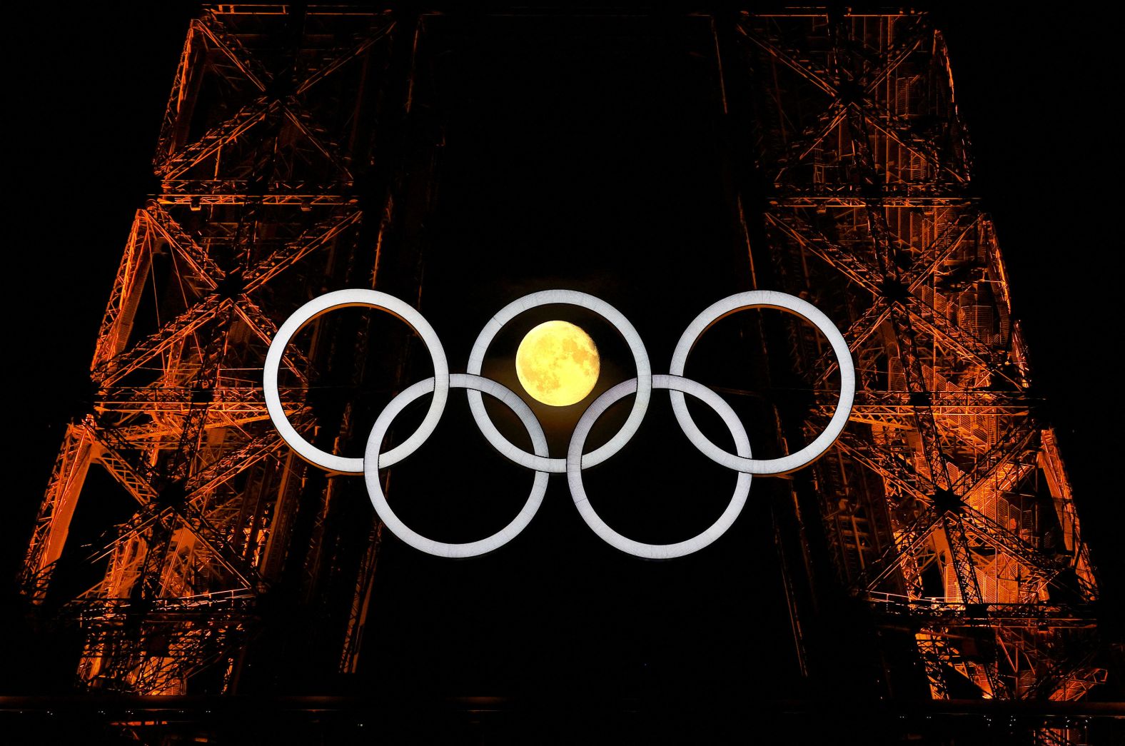 The moon is seen through the Olympic rings on Paris’ Eiffel Tower on Tuesday, July 23. <a href="https://www.cnn.com/sport/paris-olympics-2024">Paris is hosting the Olympics</a> through August 11.