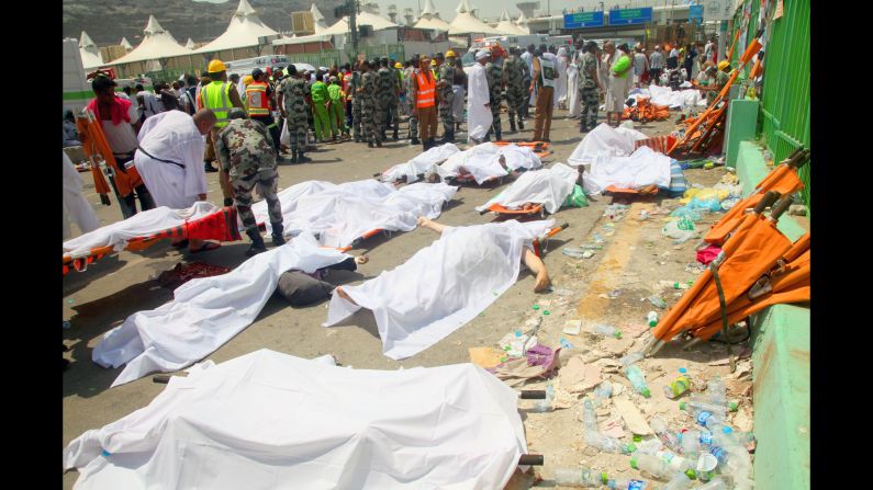 People stand near bodies covered in sheets.