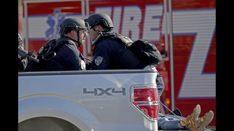 Police officers ride in the back of a pickup truck as they tend to a victim.