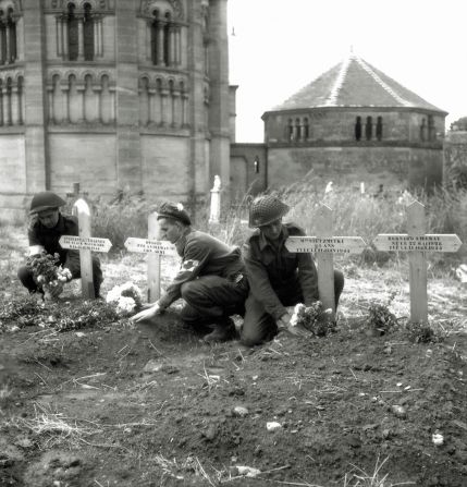 Canadian soldiers place flowers on temporary graves for allied soldiers in Normandy.