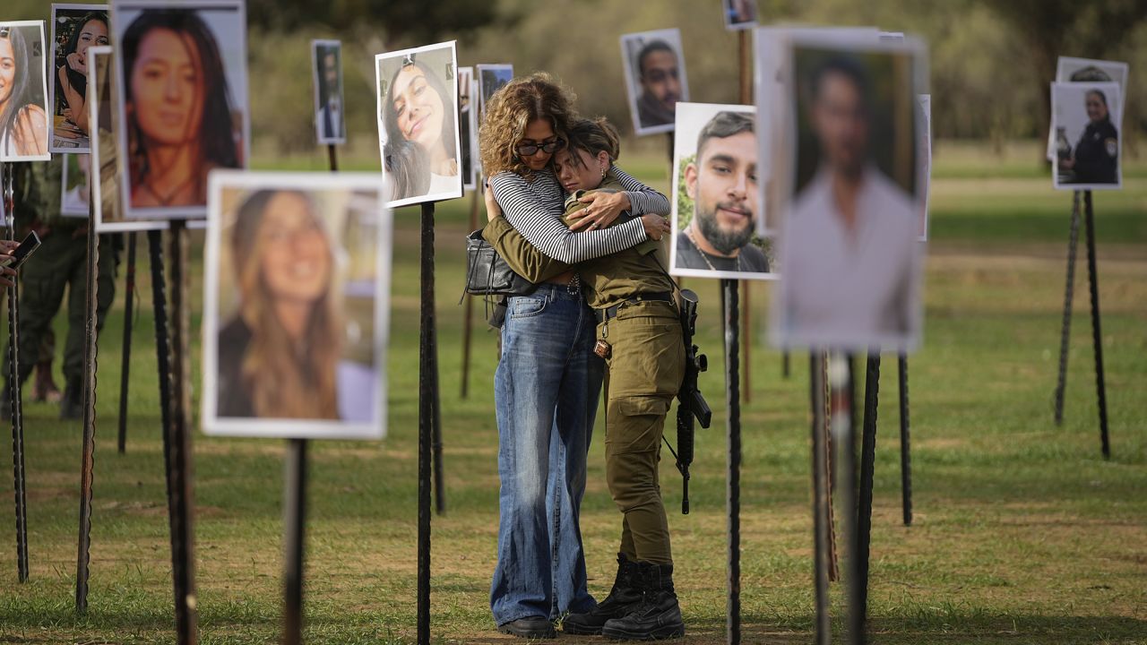 Israelis embrace next to photos of people killed and taken captive by Hamas militants during their violent rampage through the Nova music festival in southern Israel, which are displayed at the site of the event, as Israeli DJs spun music, to commemorate the October 7, massacre, near kibbutz Re'im, Tuesday, Nov. 28, 2023. (AP Photo/Ohad Zwigenberg)