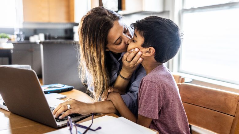 Mother working from home at kitchen table while son gets her attention