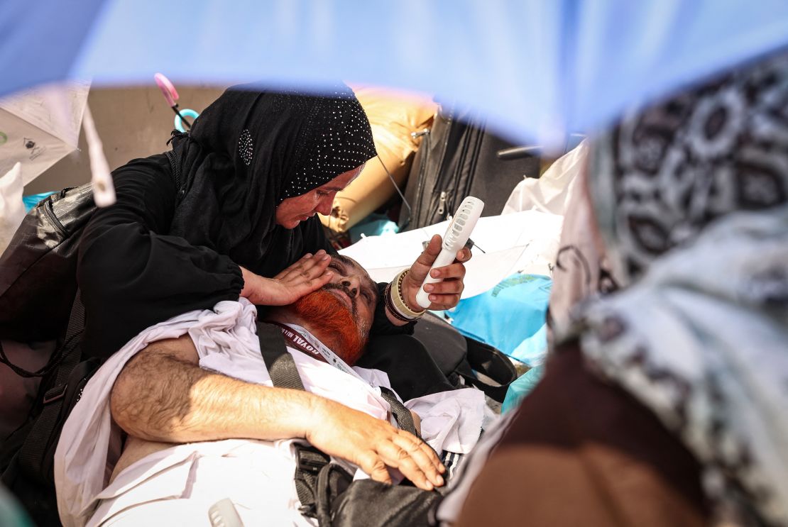 A woman uses a hand held battery run fan to cool off a man lying on the ground during the symbolic 'stoning of the devil' ritual at the annual hajj pilgrimage in Mina on June 16, 2024.