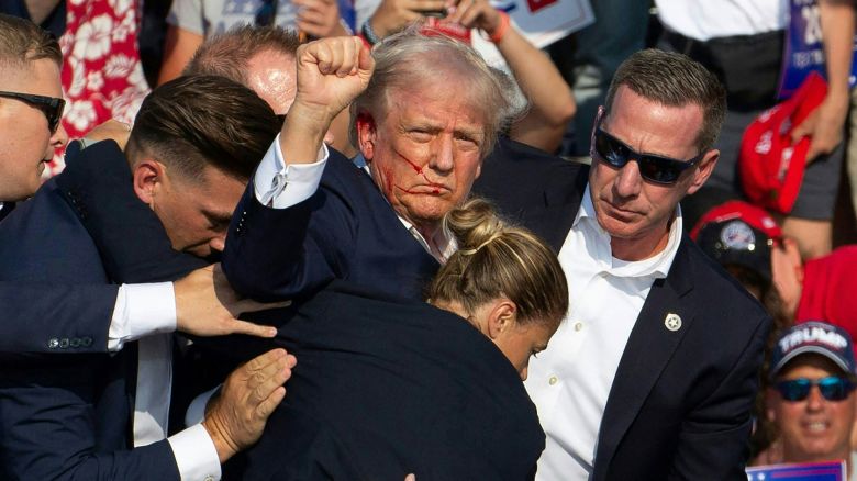 TOPSHOT - Republican candidate Donald Trump is seen with blood on his face surrounded by secret service agents as he is taken off the stage at a campaign event at Butler Farm Show Inc. in Butler, Pennsylvania, July 13, 2024. Donald Trump was hit in the ear in an apparent assassination attempt by a gunman at a campaign rally on Saturday, in a chaotic and shocking incident that will fuel fears of instability ahead of the 2024 US presidential election. The 78-year-old former president was rushed off stage with blood smeared across his face after the shooting in Butler, Pennsylvania, while the gunman and a bystander were killed and two spectators critically injured. (Photo by Rebecca DROKE / AFP) (Photo by REBECCA DROKE/AFP via Getty Images)