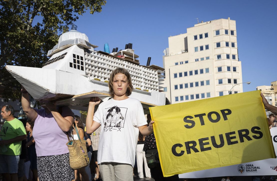 A young person holds a placard which reads as "Stop cruises," while taking part in a demonstration in Palma de Mallorca to protest against overtourism and housing prices.