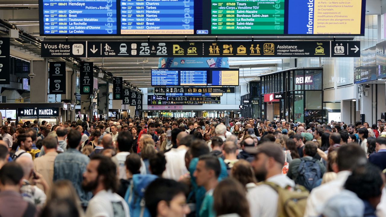 TOPSHOT - Passengers gather around the departure boards at the Gare Montparnasse train station in Paris on July 26, 2024 as France's high-speed rail network was hit by malicious acts disrupting the transport system hours before the opening ceremony of the Paris 2024 Olympic Games. According to SNCF a massive attack on a large scale hit the TGV network and many routes will have to be cancelled. SNCF urged passengers to postpone their trips and stay away from train stations. (Photo by Thibaud MORITZ / AFP) (Photo by THIBAUD MORITZ/AFP via Getty Images)