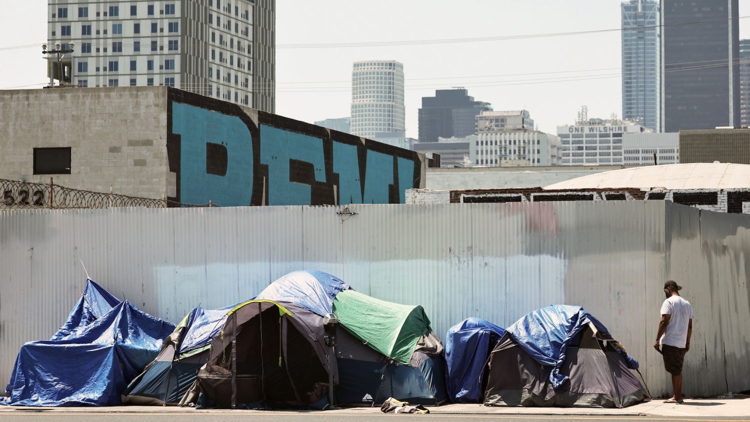 A person stands near an encampment of homeless people in the Skid Row community on July 25, 2024 in Los Angeles, California.