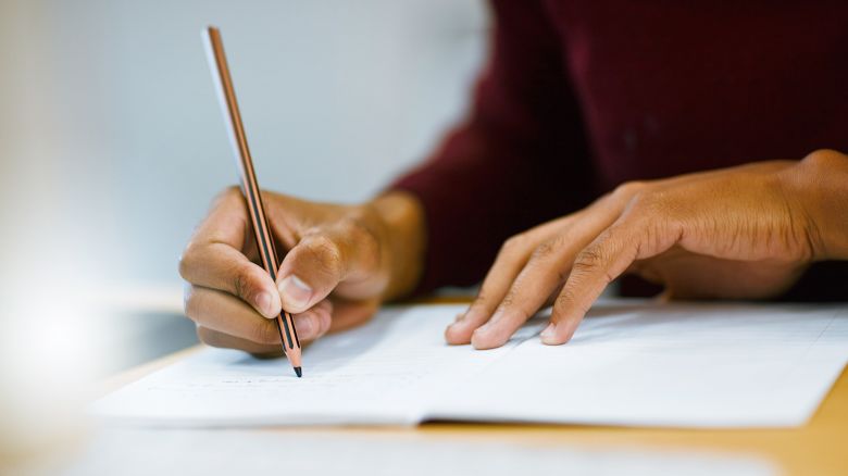 Shot of a unrecognizable student writing down notes while working on a computer in a library